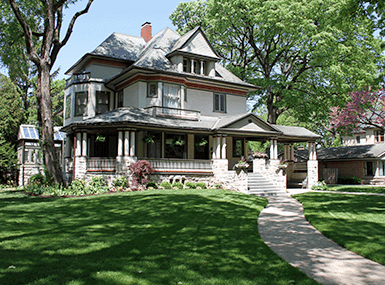 Nice large house surrounded by tall trees and well-maintained lawn with pathway.