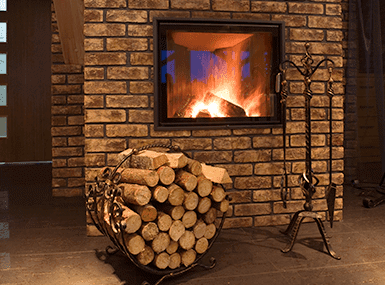Modern brick and glass-covered fireplace with a pile of wood and fire pokers beside it.