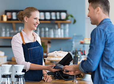 Smiling customer and store clerk processing a purchase using a payment device at a cafe.