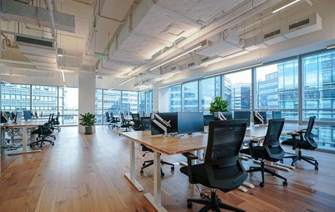 Inside of a glass office building full of tables, office chairs, and computer monitors.